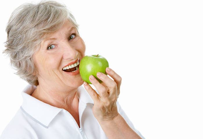 Grey haired lady with dentures about to bite into an apple